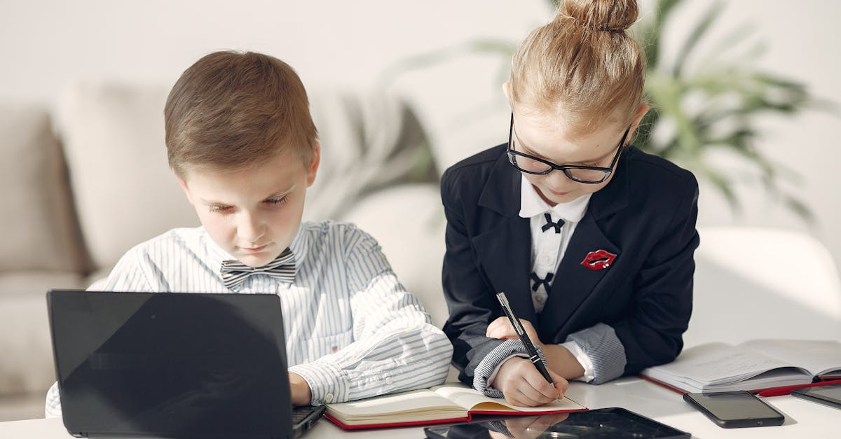 Two children dressed professionally using laptops and tablets indoors.