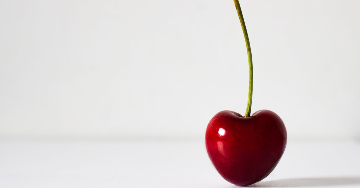 A vibrant red cherry with a long stem on a clean white surface, highlighting freshness and simplicity.