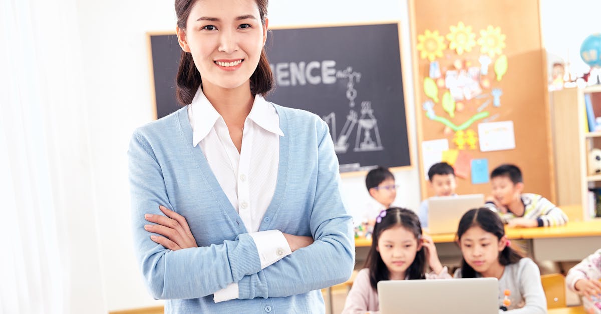 Smiling teacher posing in a classroom with engaged students on laptops.