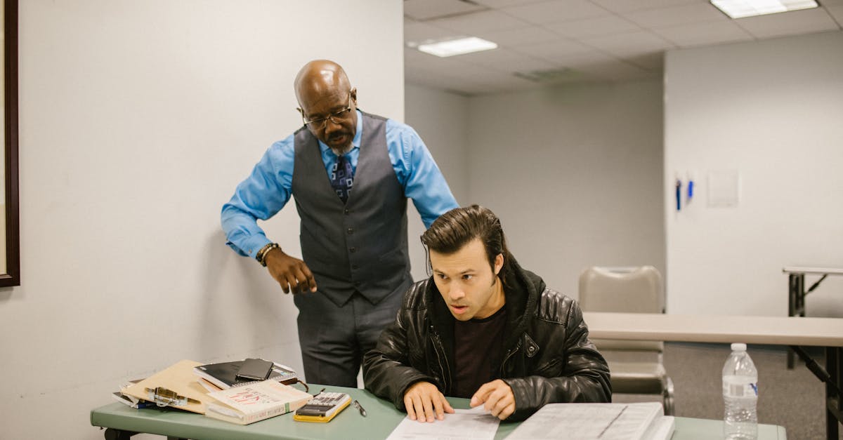 A teacher reprimands a student caught cheating in a classroom with study materials on the desk.