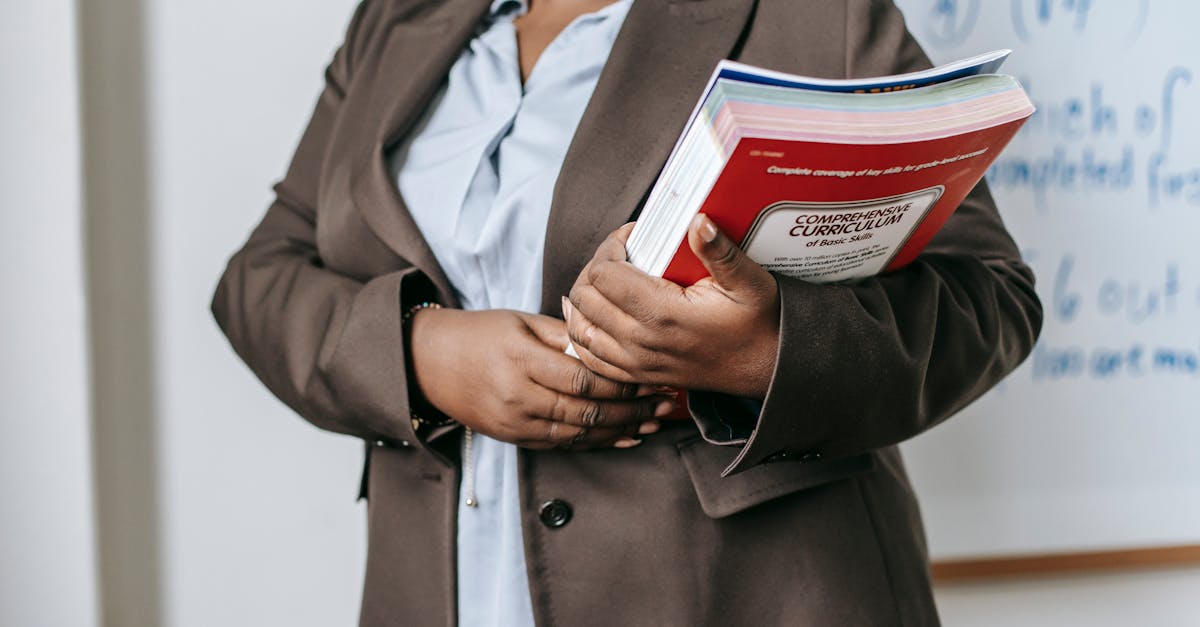 A professional educator in a formal setting holding a curriculum book in front of a whiteboard.