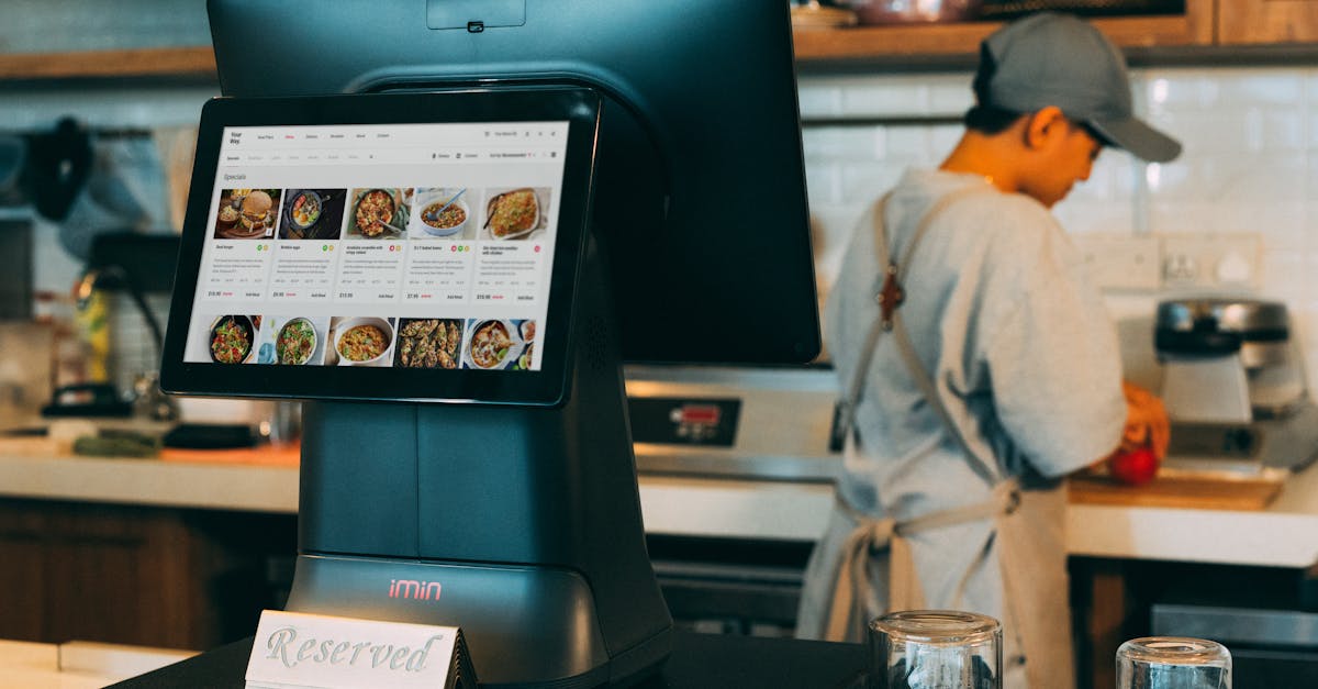 Digital ordering system in a restaurant kitchen with a touchscreen display and a chef at work.