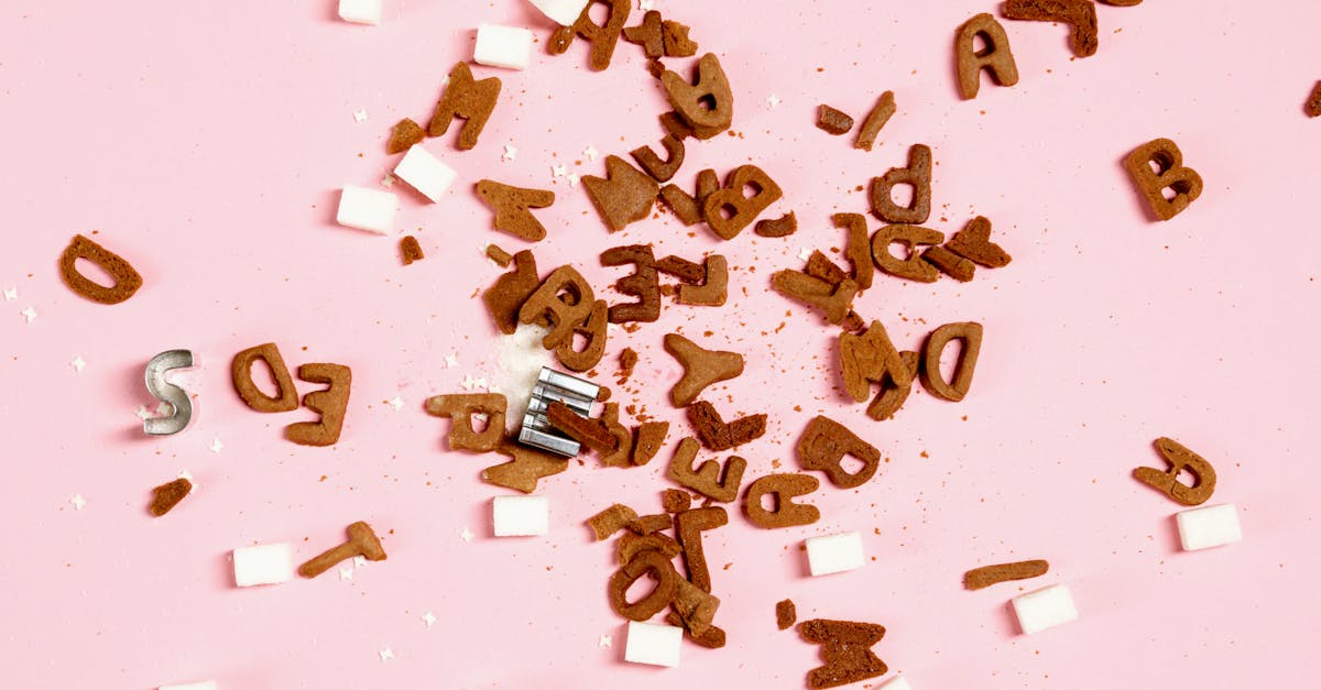 Overhead view of sugar cubes and cookie letters scattered on a pink surface, suggesting sweet chaos.