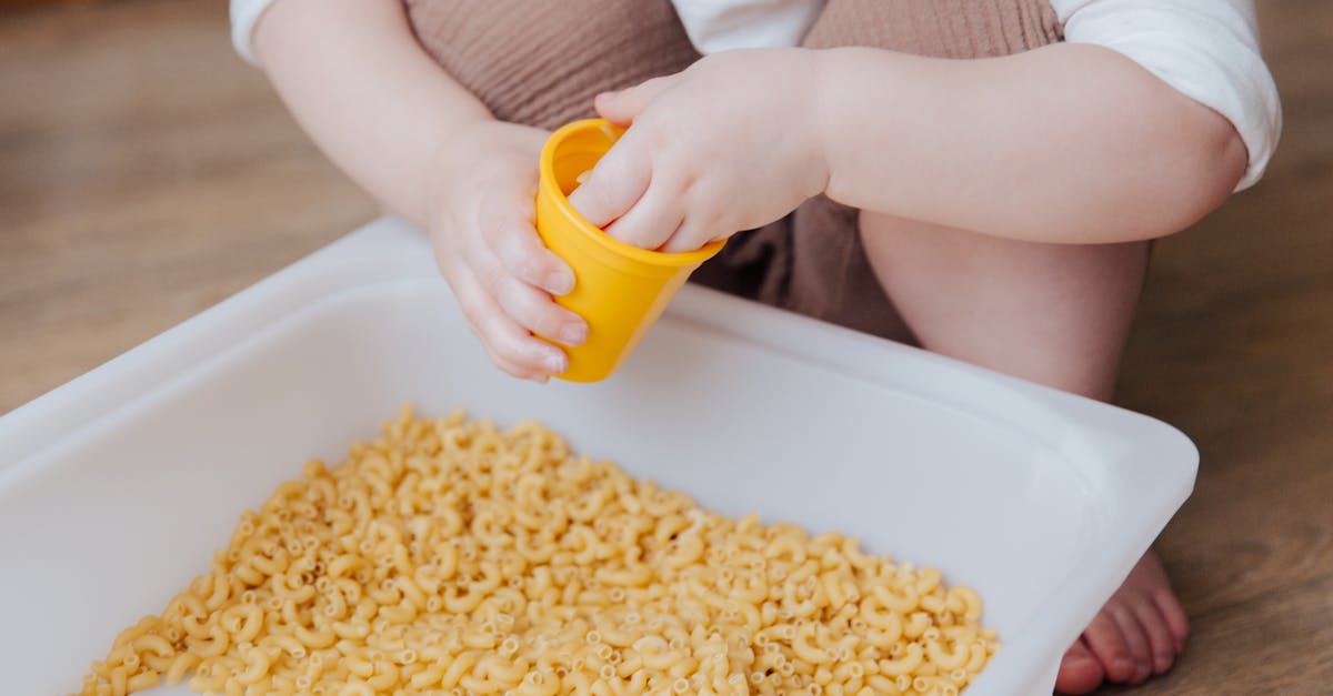 A young child plays with dry macaroni in a sensory activity, enhancing creativity and learning.