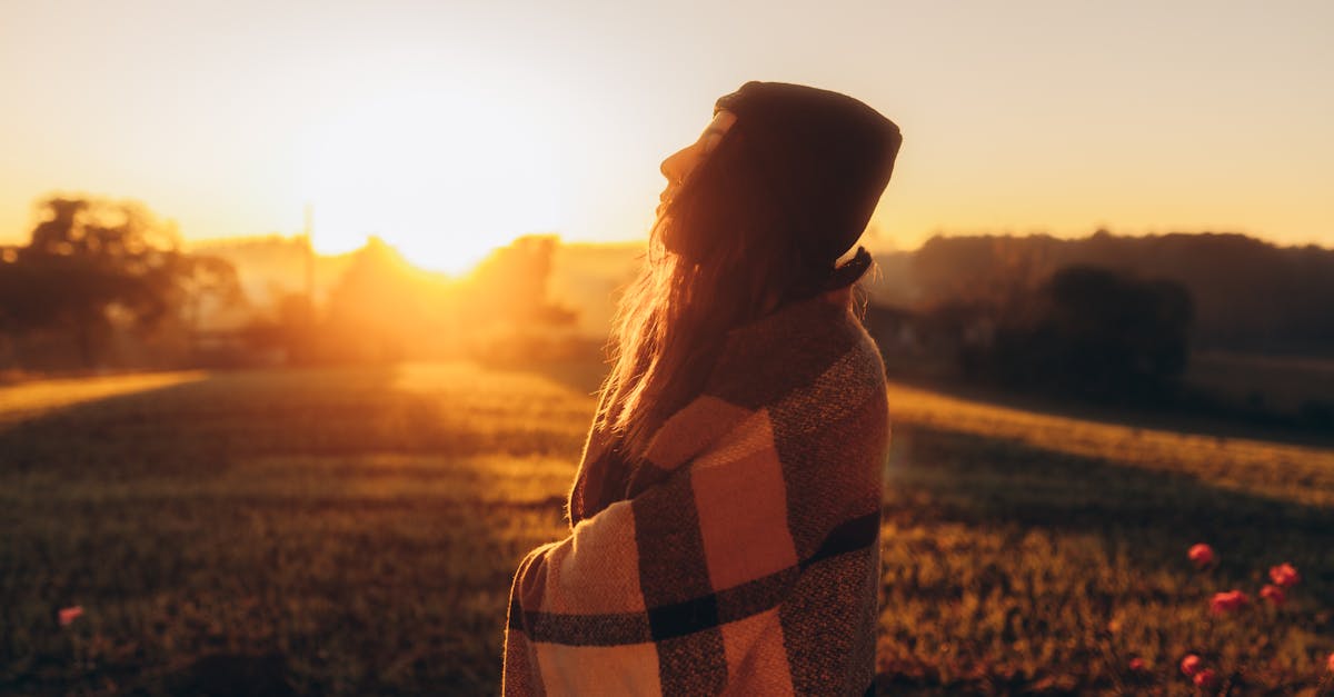 Peaceful scene of a woman wrapped in a blanket at sunrise, embracing nature's serenity.