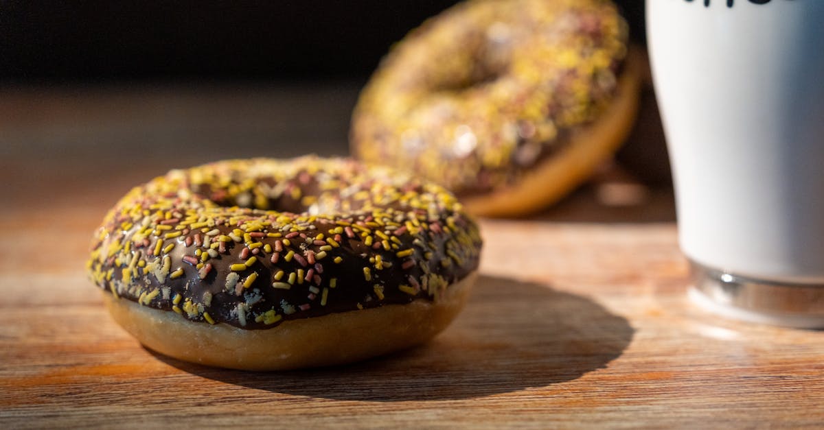 Delicious chocolate glazed doughnuts with sprinkles and a cup of coffee on a sunny wooden table.
