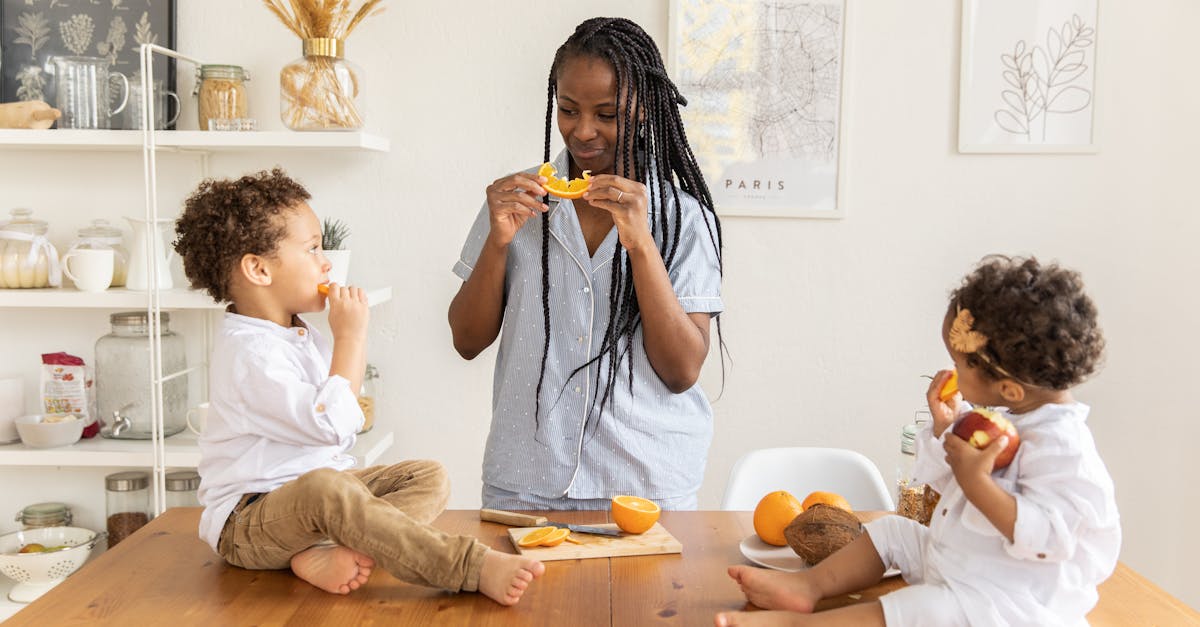 A joyful mother and her children enjoy eating fresh oranges at the kitchen table.