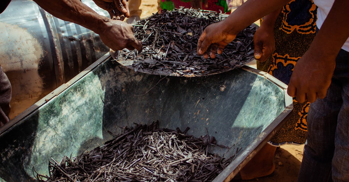 Hands of people working with charcoal in a wheelbarrow outdoors.