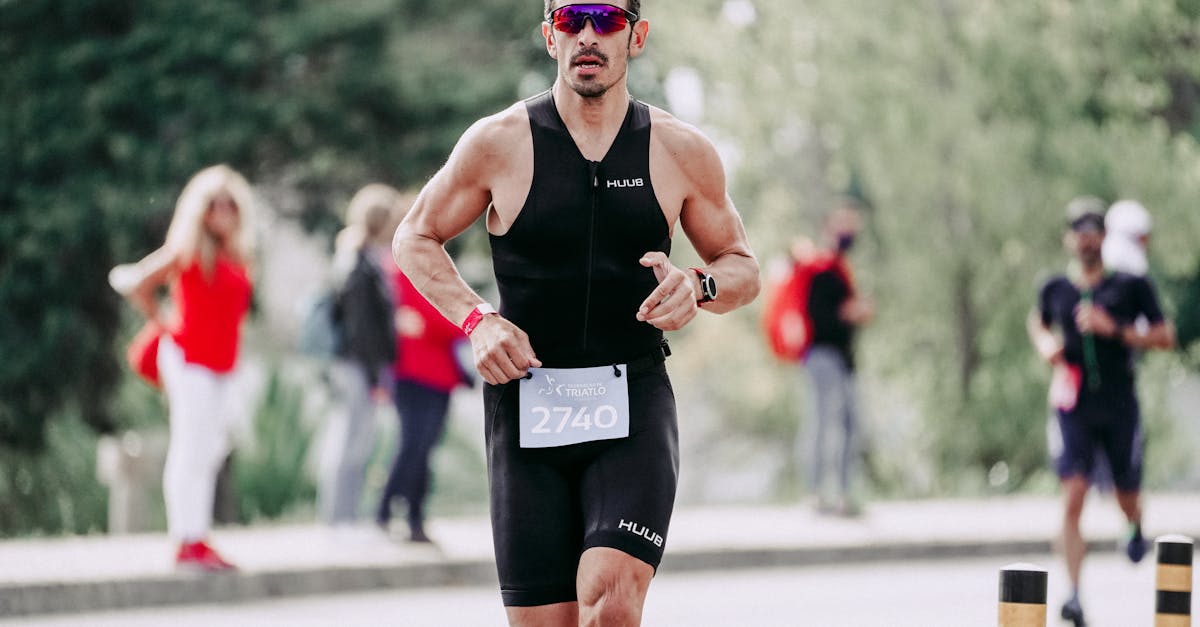 Strong muscular sportsman in sportswear and protective glasses running on asphalt road during competition
