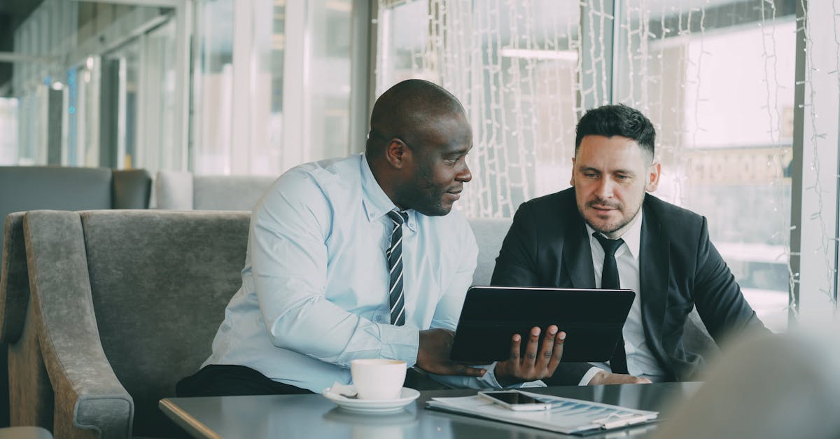 Two men in business attire collaborating over a tablet in a modern office setting.