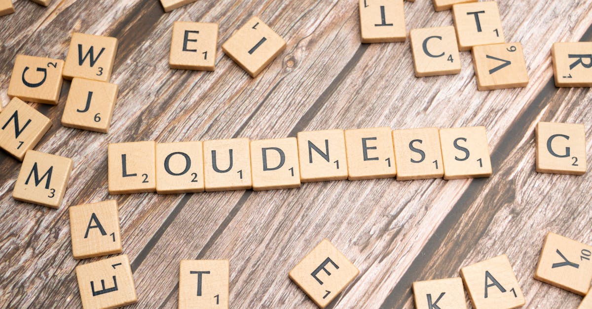Scrabble tiles spelling 'Loudness' scattered over a wooden surface, emphasizing sound themes.