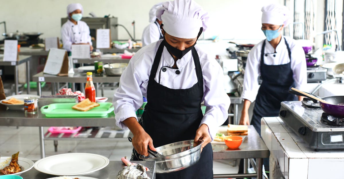 Chefs in masks preparing food in a commercial kitchen, emphasizing hygiene and teamwork.