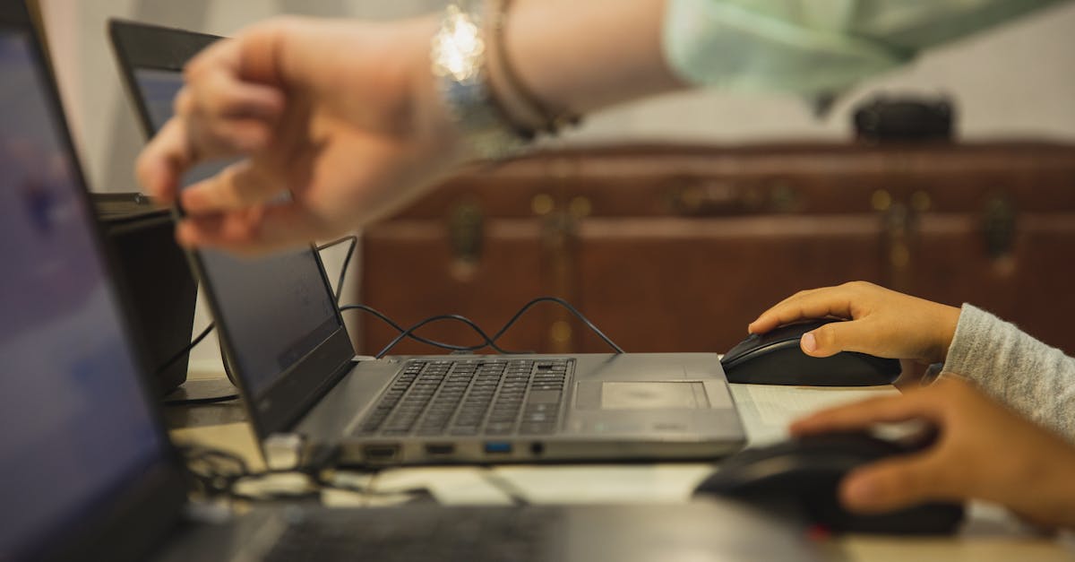 Crop anonymous female teacher pointing at netbook screen near schoolchildren touching mouses at desk in classroom