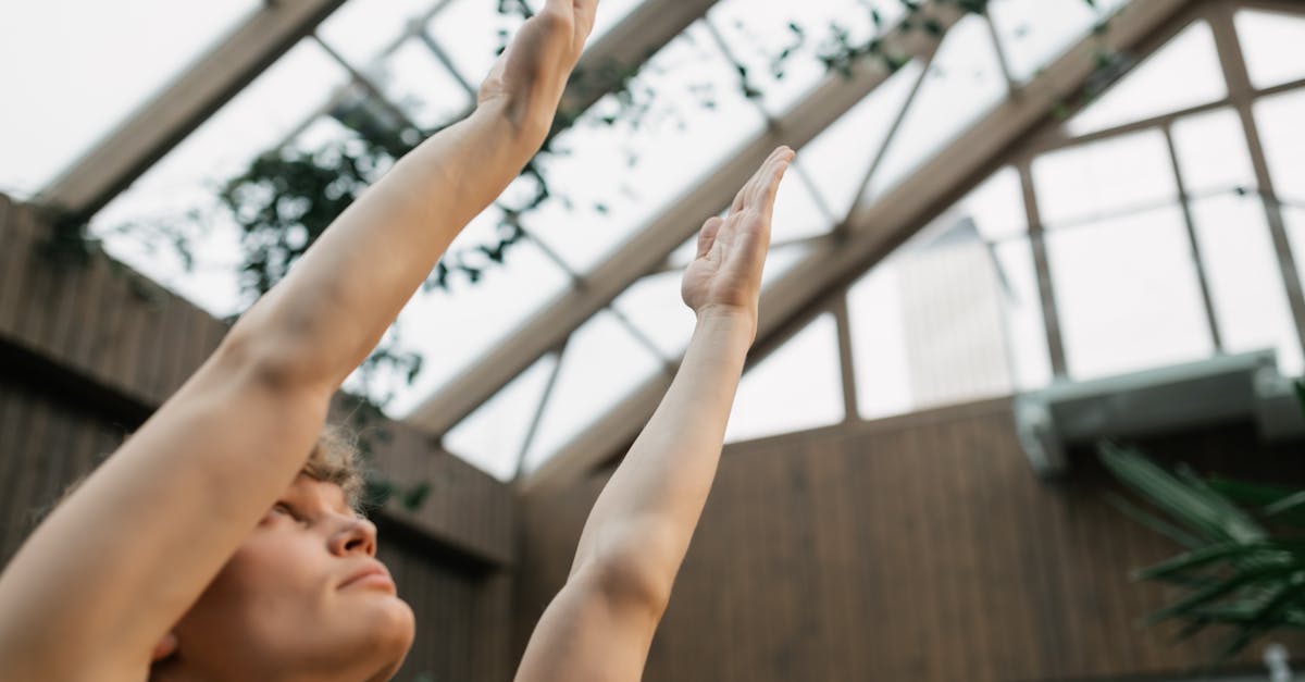 Person practicing yoga indoors with arms raised in a glass-roofed room.