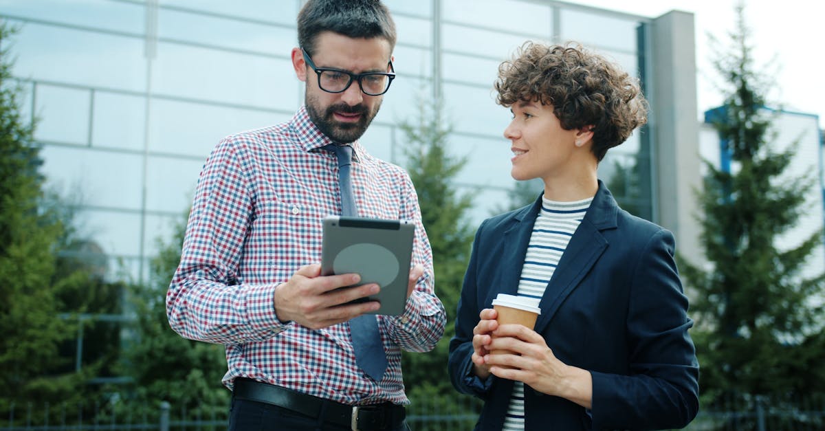 Two professionals discuss business strategies using a tablet outside a modern building.