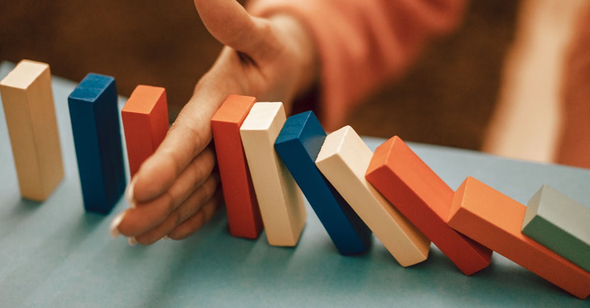 A hand strategically stops falling blue and red domino blocks on a table.
