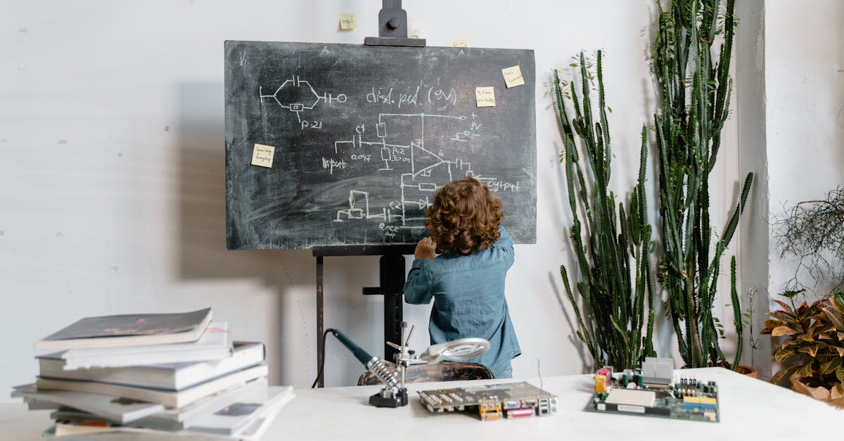 Curious young boy drawing STEM concepts on a blackboard indoors, surrounded by educational materials.