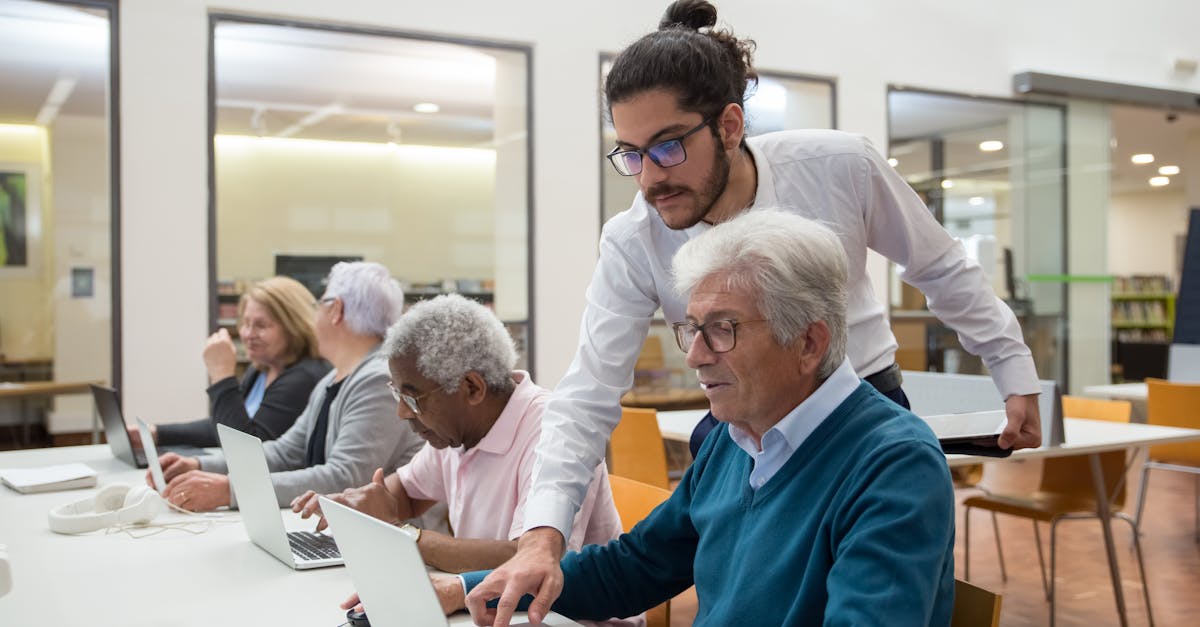 A teacher guiding senior adults in a library, using laptops for learning and support.