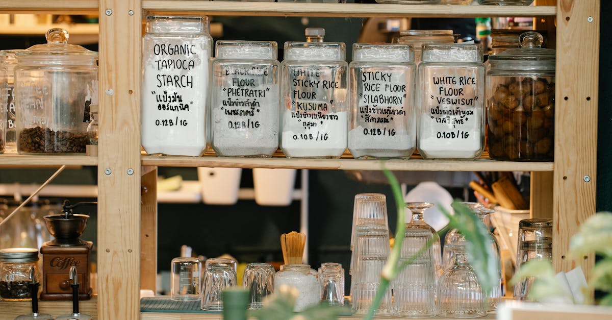 Collection of various glass jars with different dry food and glassware placed on wooden shelf