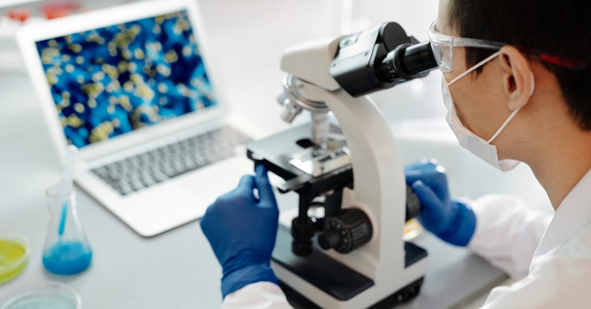 Scientist examining samples under a microscope in a lab with laptop display.