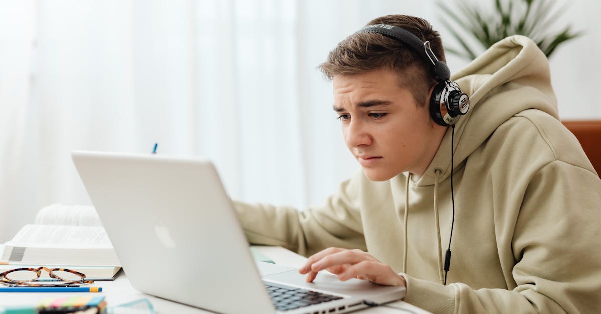 Teen wearing headphones studies online with a laptop in a cozy indoor setting.