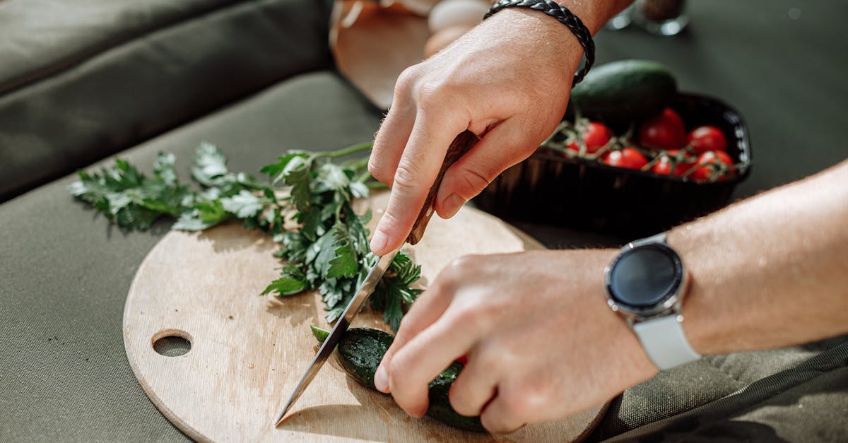 Hands cutting cucumbers and parsley with cherry tomatoes nearby on a wooden board.