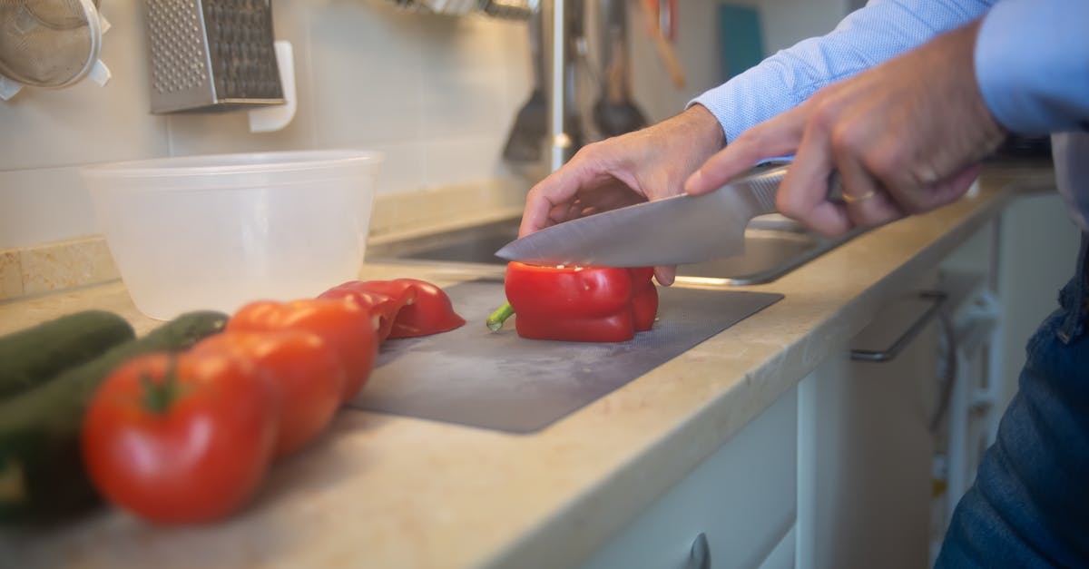 A man slices red bell peppers and tomatoes on a kitchen counter with a knife.