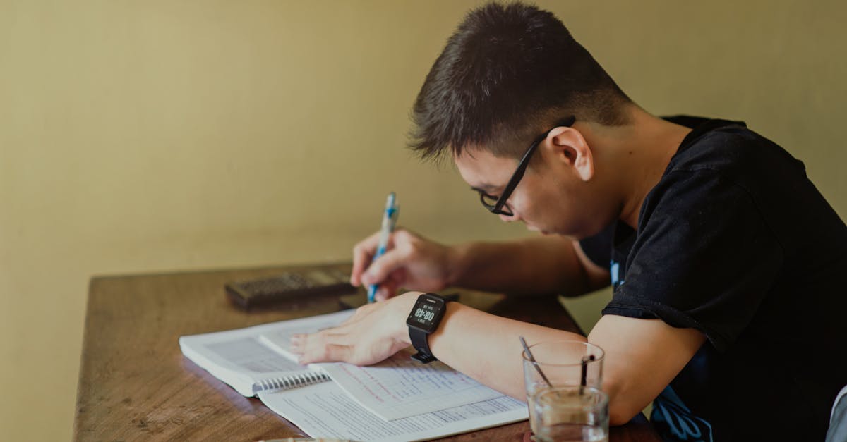 A young man concentrates on studying at his desk, taking notes indoors.
