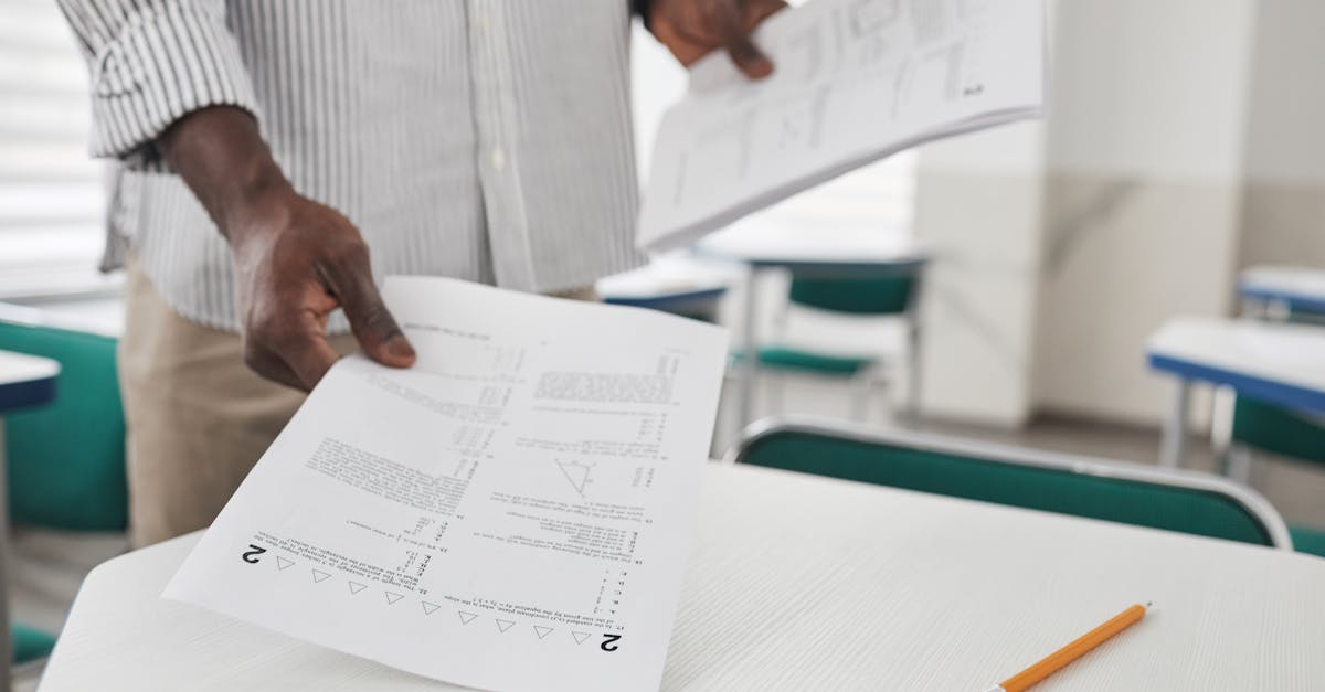 Close-up of a person arranging examination papers on a desk in a classroom.
