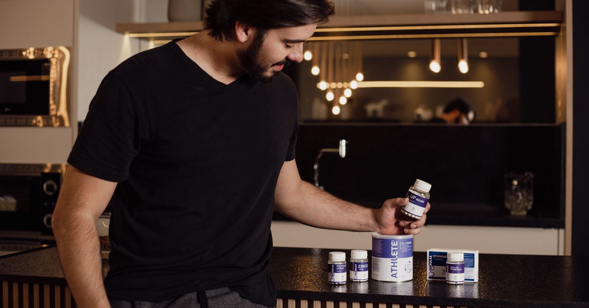 Adult man in modern kitchen examining various health supplements for fitness and wellness.