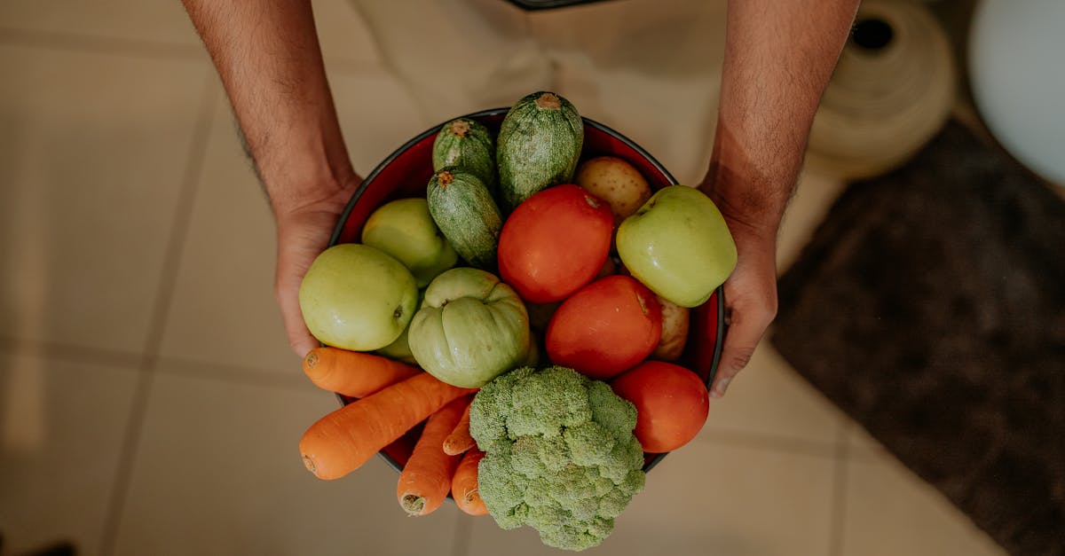 A variety of colorful fresh vegetables held in a bowl by a man's hands, showcasing healthy eating.