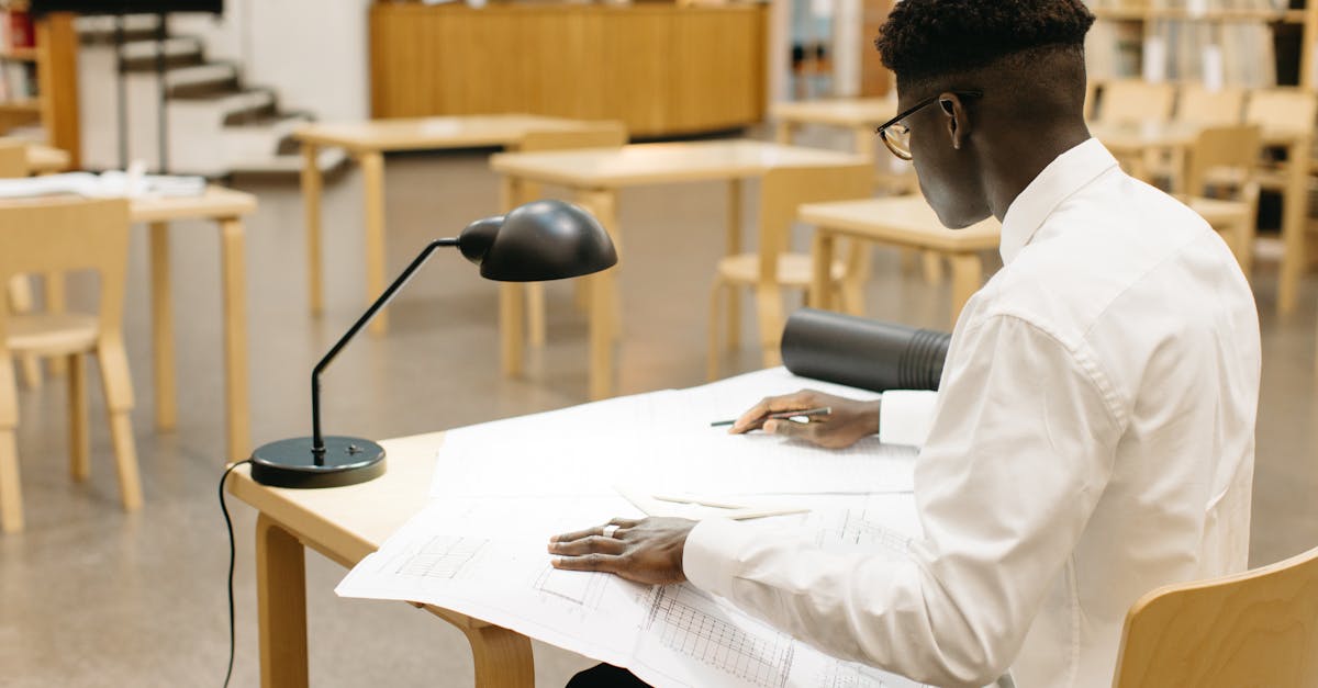 Young man drafting architectural plans at a library table, focused on work.
