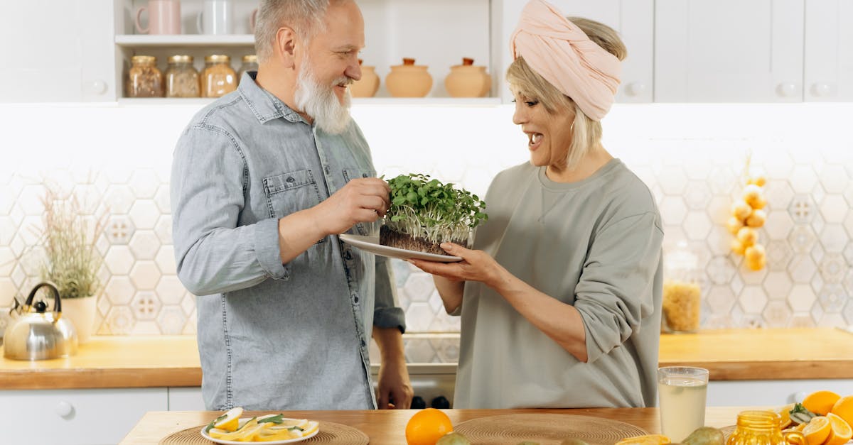 Happy senior couple smiling and holding a plate of fresh microgreens in a cozy kitchen setting.