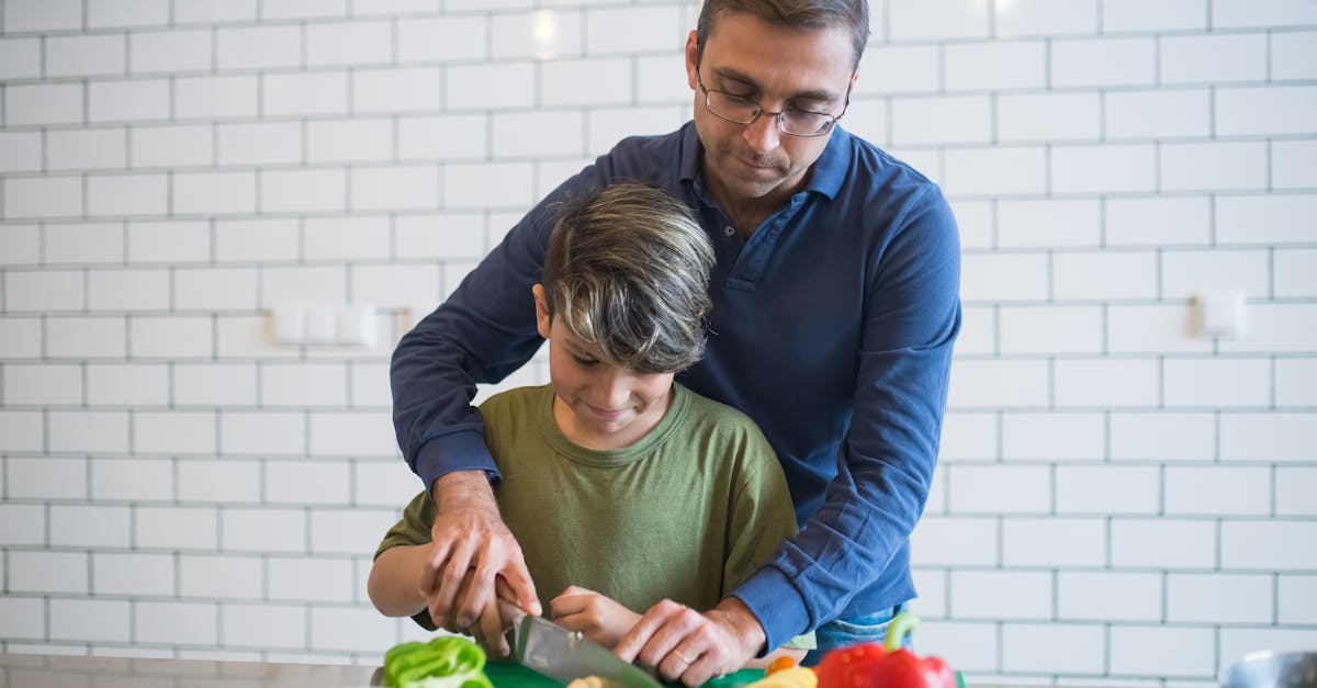 Father guides son in slicing vegetables, creating a bonding experience in a modern kitchen.