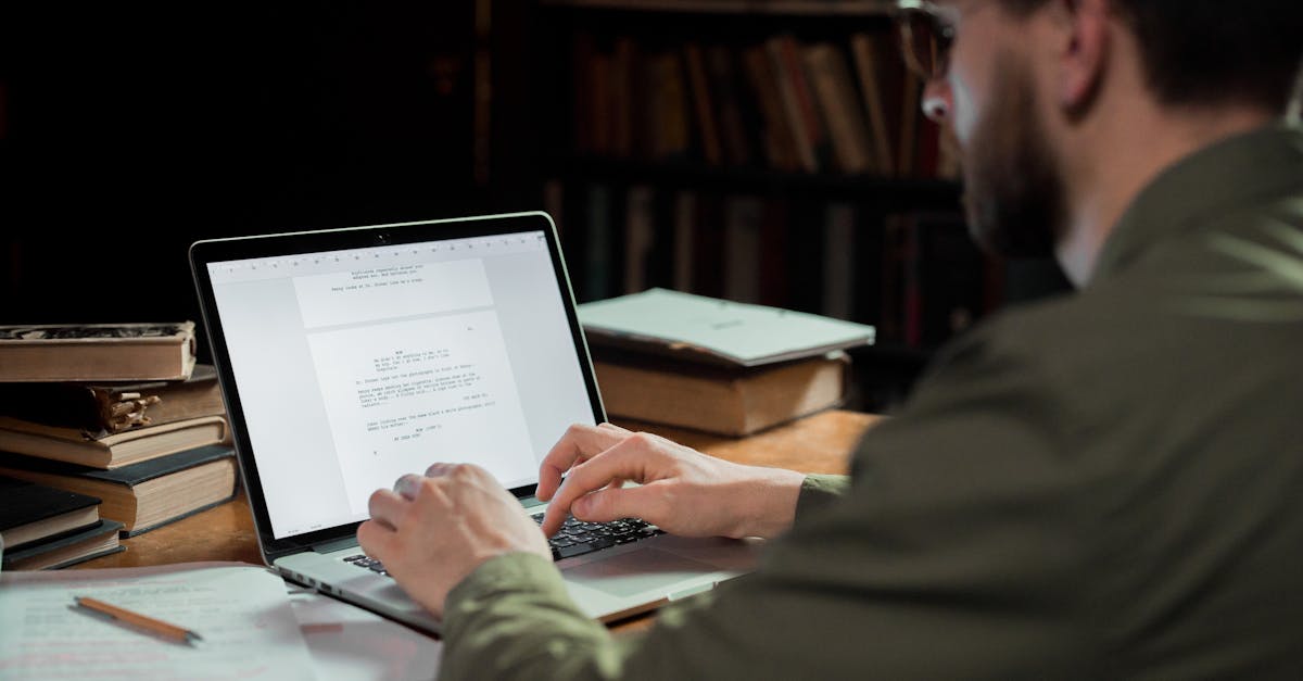 A man focuses on typing a document in a warm, cozy library environment, surrounded by books.