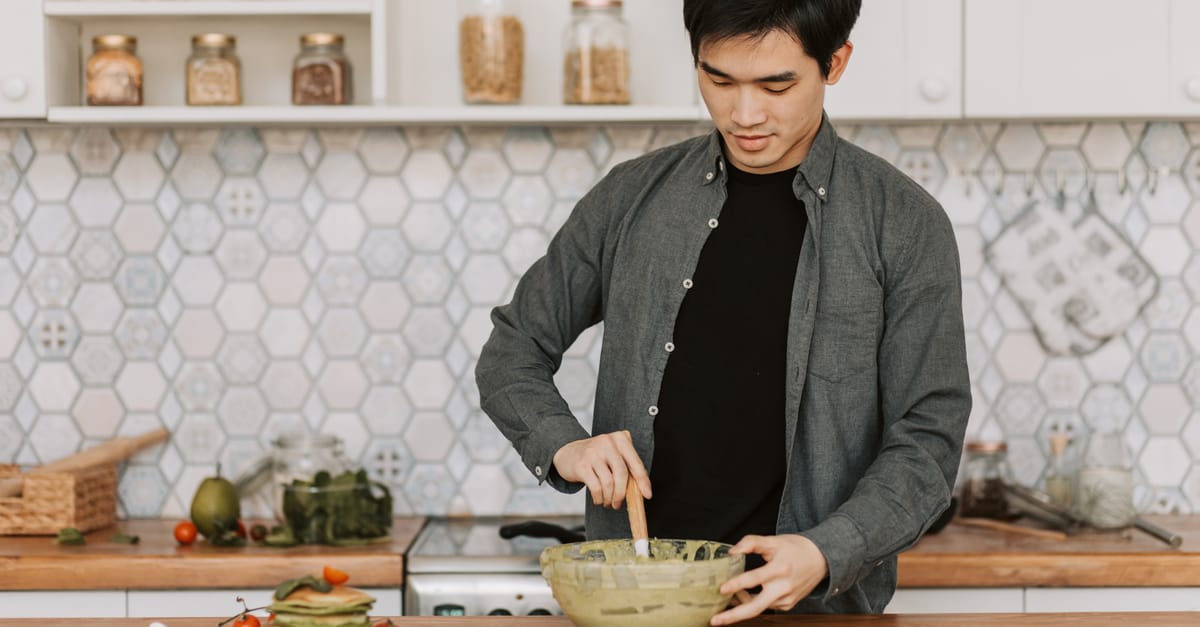 A young man stirs batter in a bowl in a stylish kitchen setting, emphasizing home cooking.