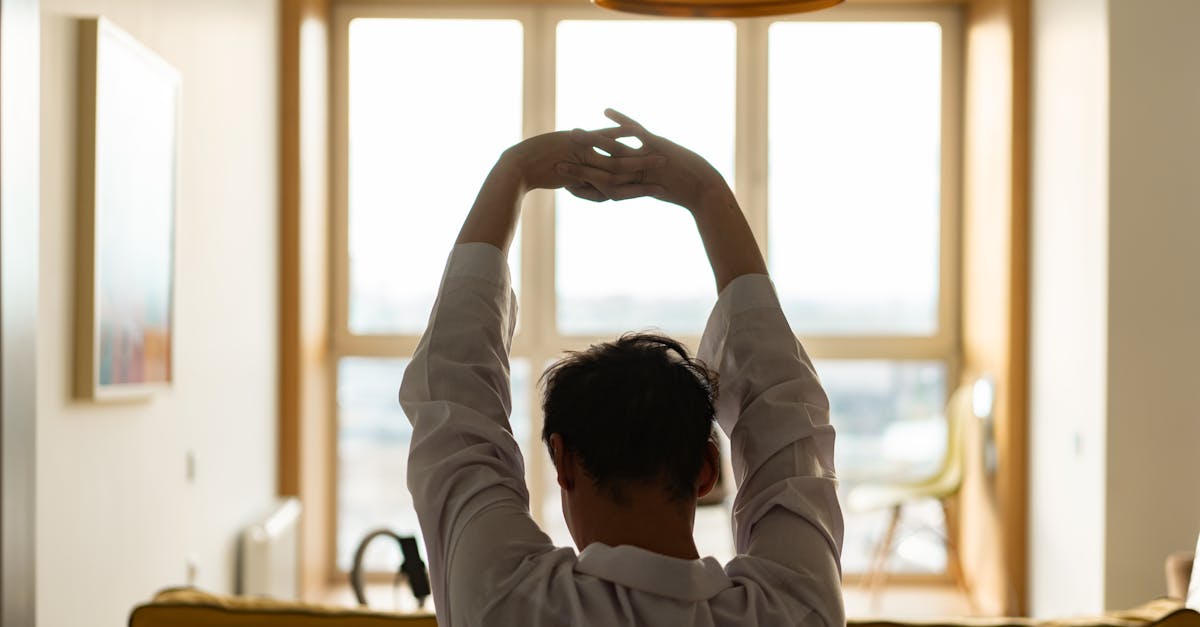 Back view of a man stretching inside a room with a sunny window backdrop.