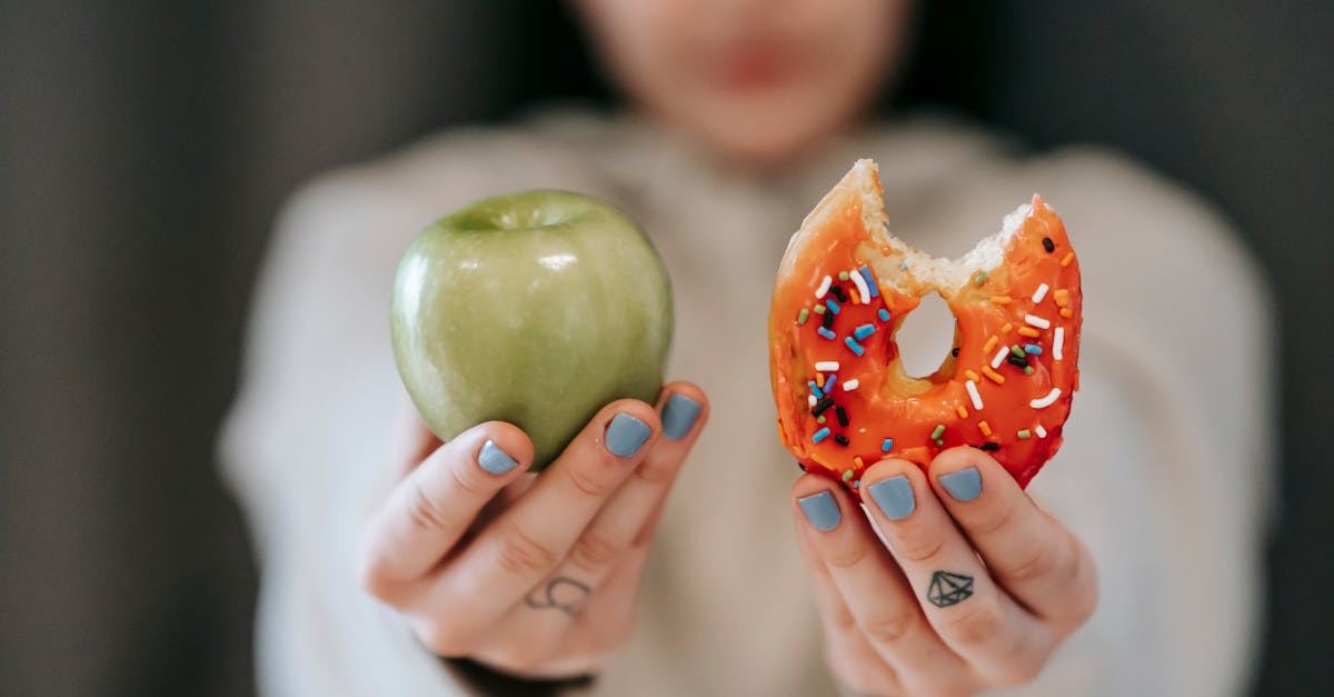 Crop anonymous female demonstrating delicious sweet donut and fresh green apple while making decision