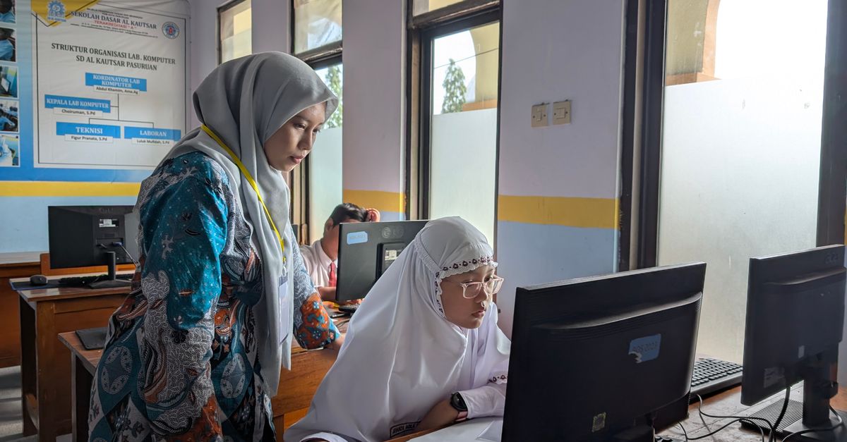 A female teacher guides a student working on a computer in a school lab, fostering learning.