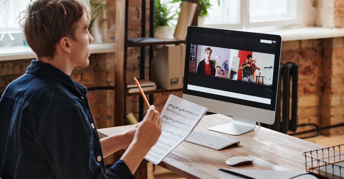 Adult male taking an online violin lesson with sheet music and computer.