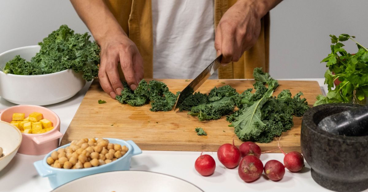 A person chops fresh kale surrounded by vibrant vegetables for a healthy meal preparation in a kitchen.