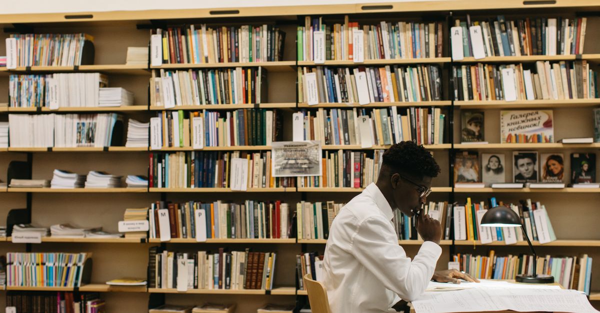 A man studying intently in a library filled with shelves of books, creating a thoughtful atmosphere.