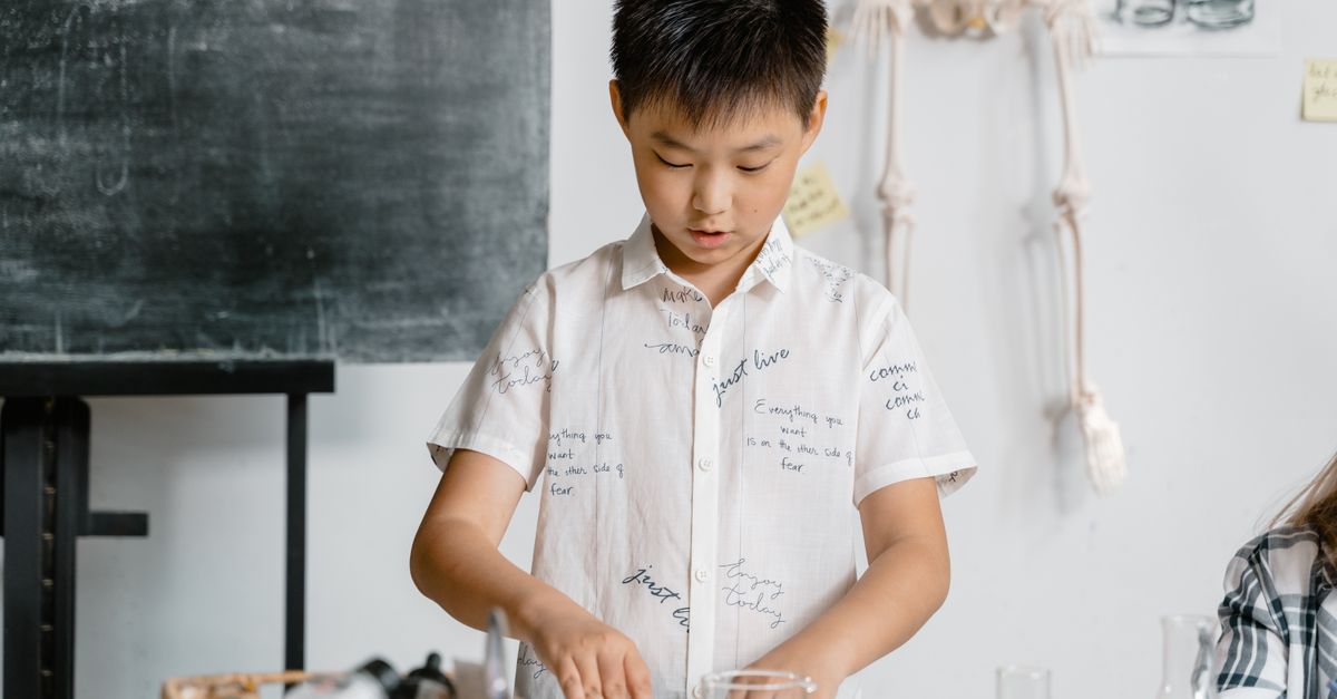 Boy in a classroom conducting a science experiment, wearing a white shirt.