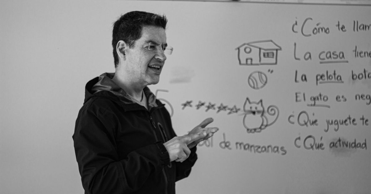 A Spanish teacher explaining language concepts on a whiteboard in class.