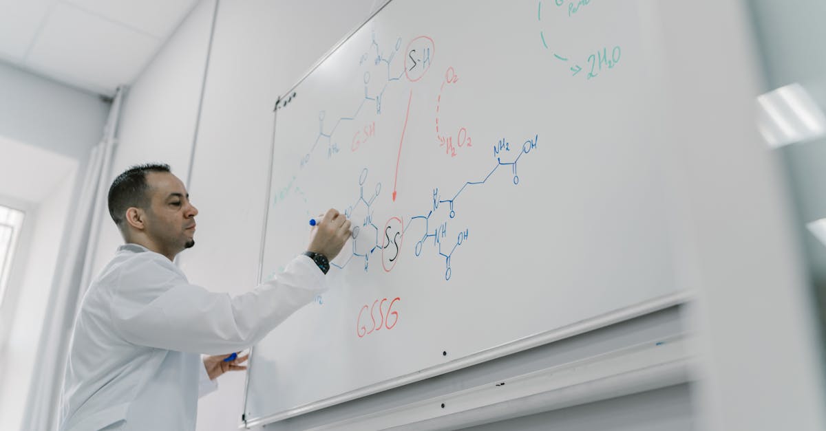 Male teacher explains chemical equation on whiteboard in science classroom setting.