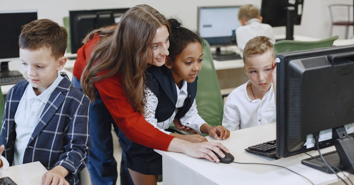 Teacher engaging with diverse children in a technology lesson using computers in a modern classroom.