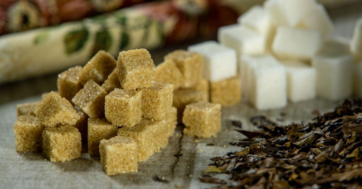 Close-up of brown sugar cubes, white sugar cubes, and tea leaves on a wooden surface.