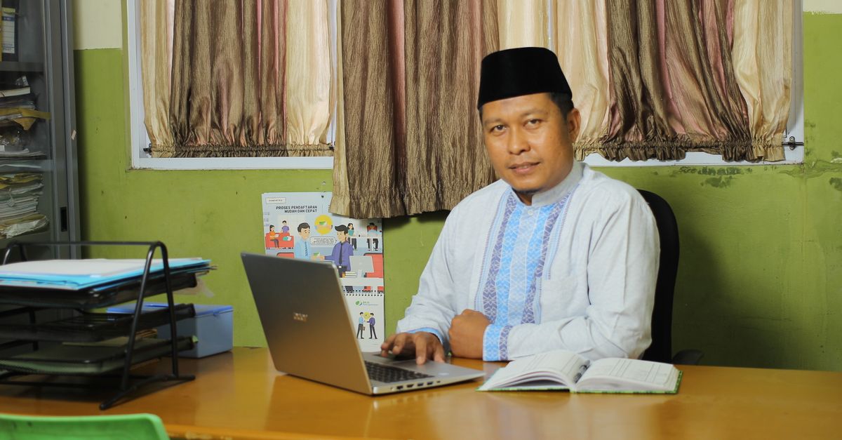 Successful Indonesian teacher working at a desk in a traditional outfit.