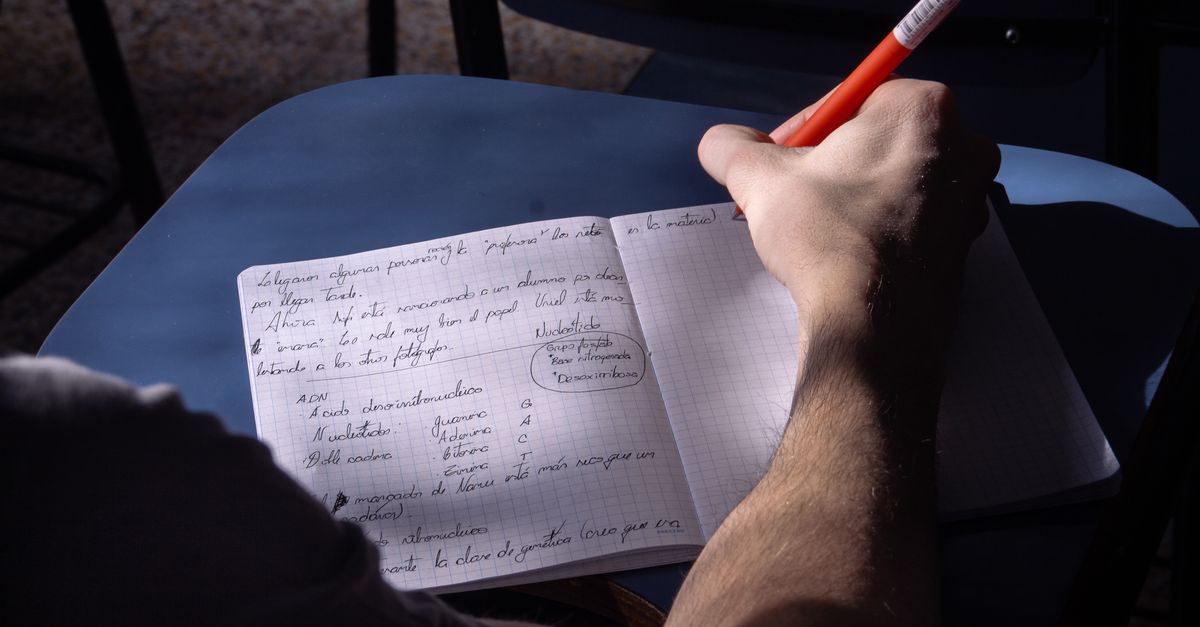 A student takes notes in a classroom in Buenos Aires. Natural lighting highlights the writing process.