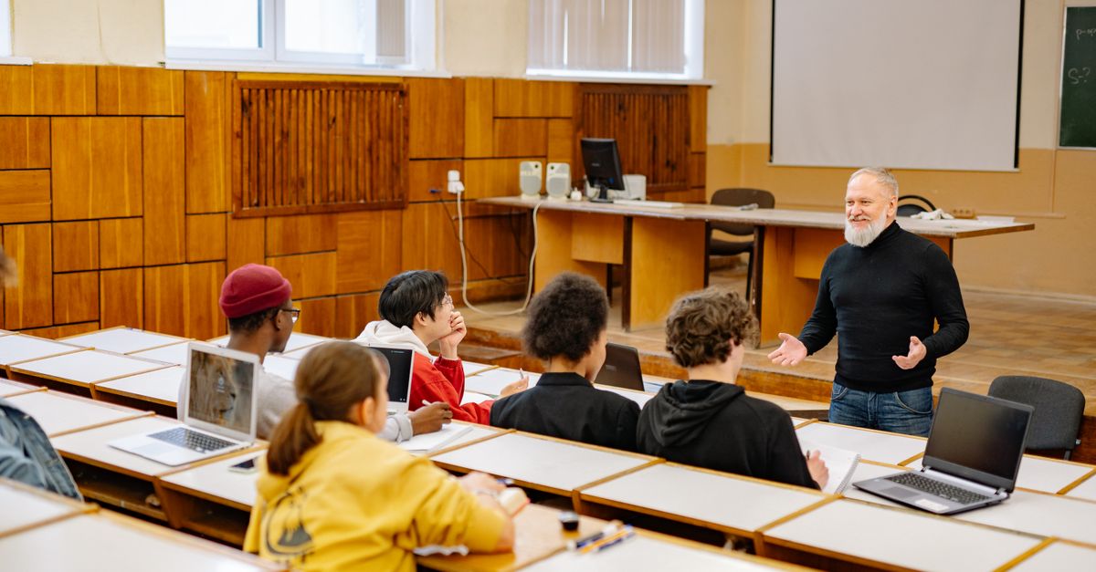 Students engaging with a professor in a university lecture hall, utilizing technology.